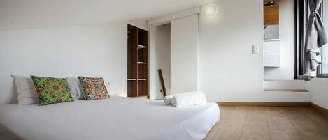 A bedroom with a large bed, a wooden wardrobe, a window with curtains, and a built-in shelf.