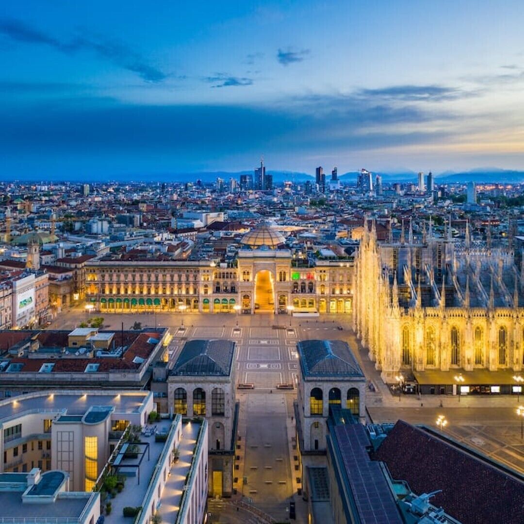 Een groot, historisch gebouw met een centrale binnenplaats en een statig entree, omringd door moderne gebouwen en een stadsachtergrond.