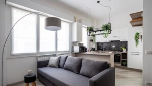 Un soggiorno moderno con un divano grigio, una lampada da terra e vista sull'area cucina.
