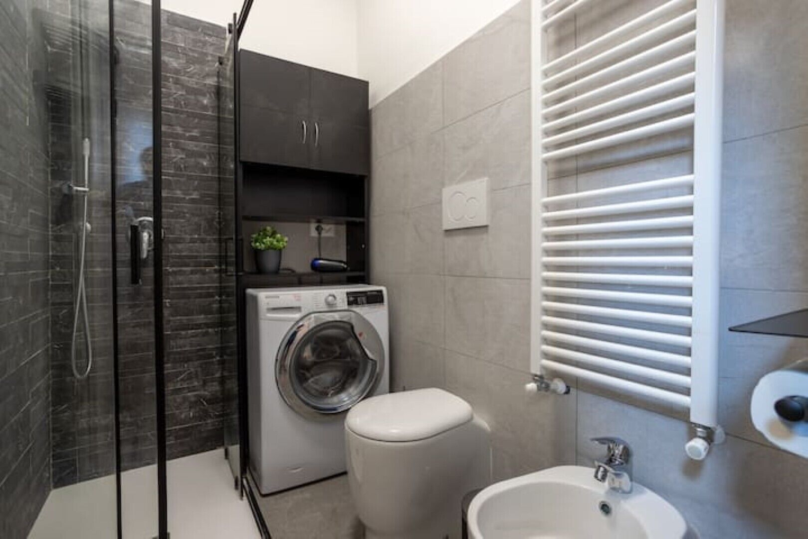 A modern bathroom with a glass shower enclosure, a built-in washing machine, a toilet, and a sink.