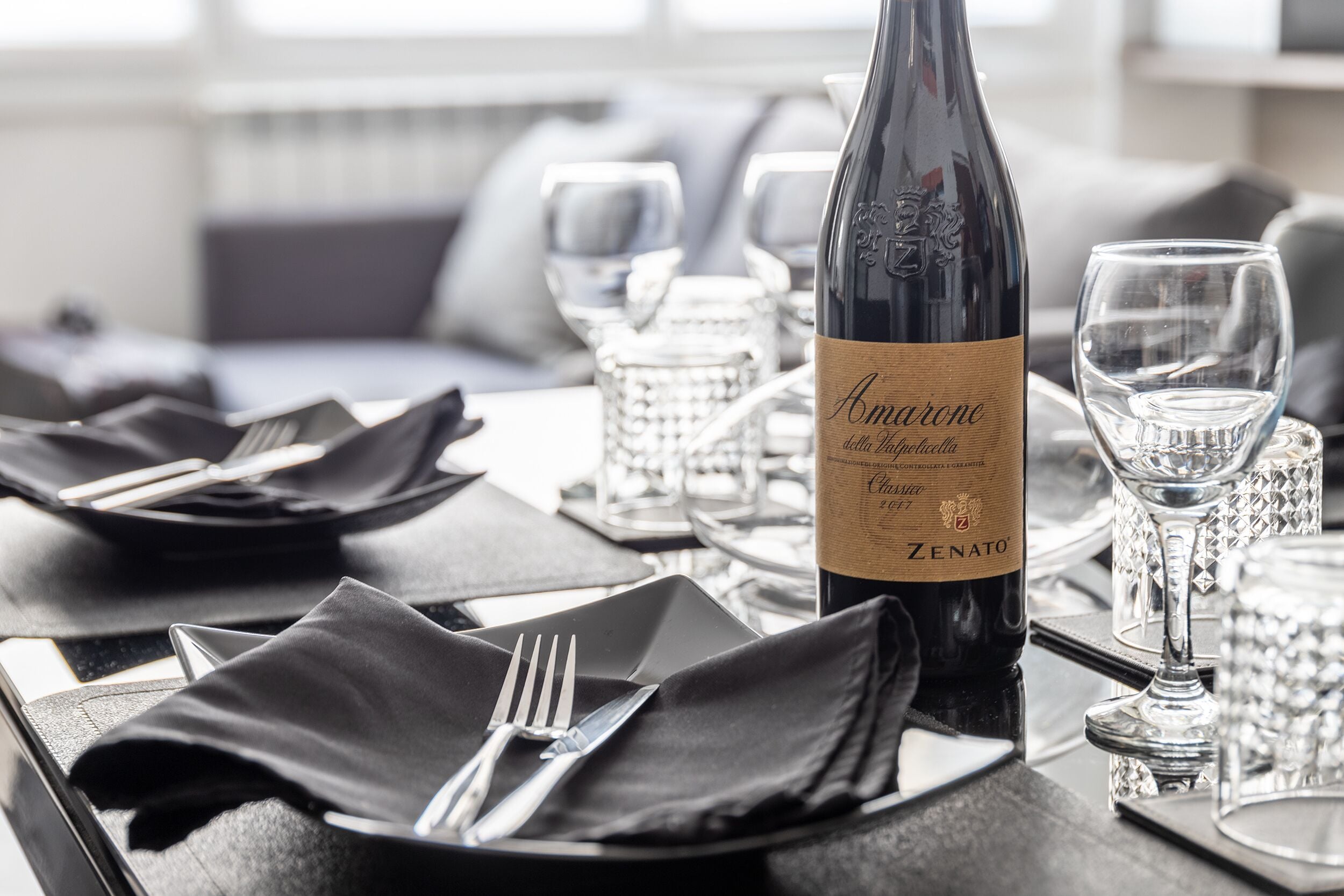 A dining table set with a bottle of Amarone wine, glasses, and cutlery.