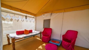 A tented room with a bed, two red chairs, and a small table with a pink ottoman. - The Captain Desert Camp (Jaisalmer)