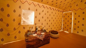 A tented room with patterned walls, a wooden bench, a small table with a bottle, and a mirror.