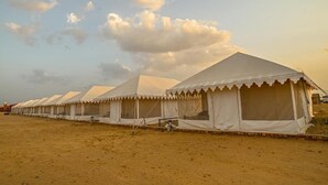 A row of white tents with a flat roof, arranged in a line on a sandy ground.