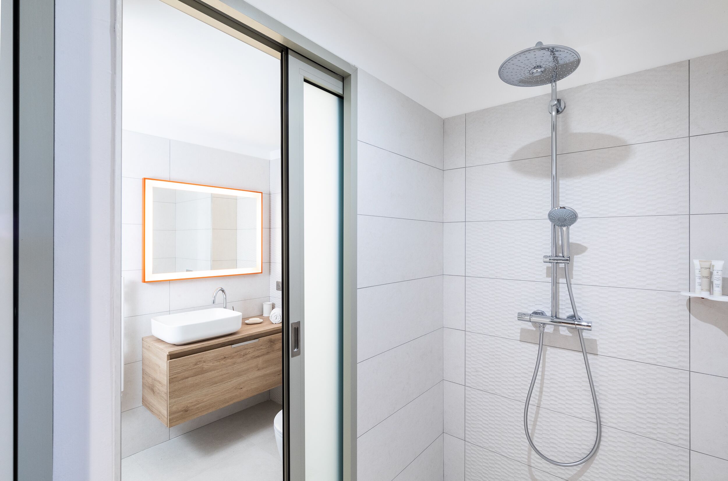 A modern bathroom with a glass door, a white sink, a wooden vanity, and a shower with a handheld showerhead.