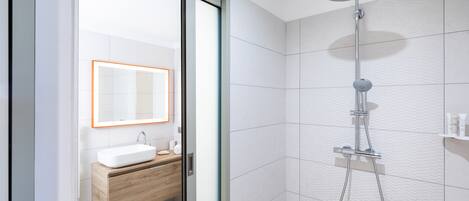 A modern bathroom with a glass door, a white sink, a wooden vanity, and a shower with a handheld showerhead.