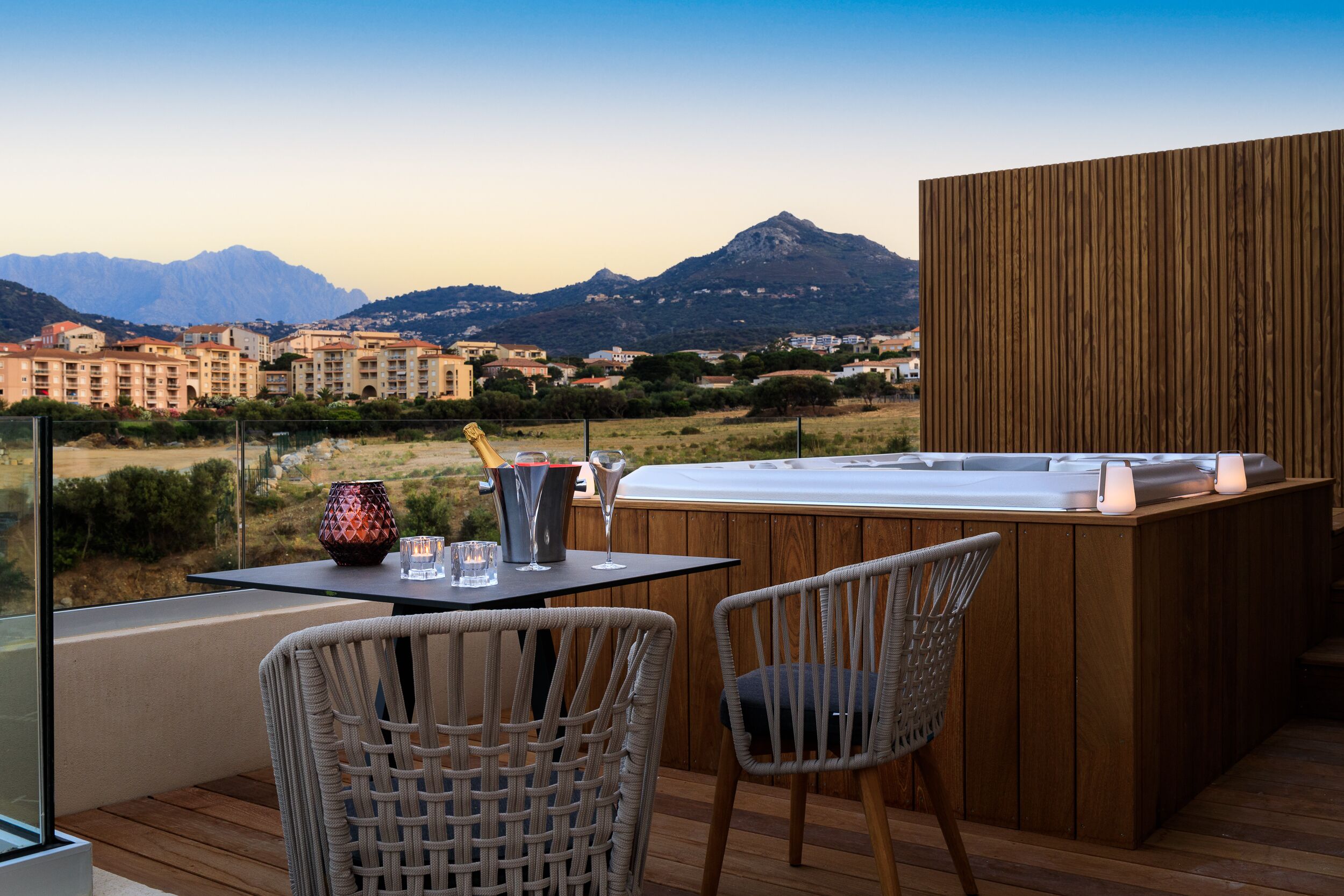Un balcon avec des fauteuils en osier, un jacuzzi et une table agrémentée d’un vase et de verres.