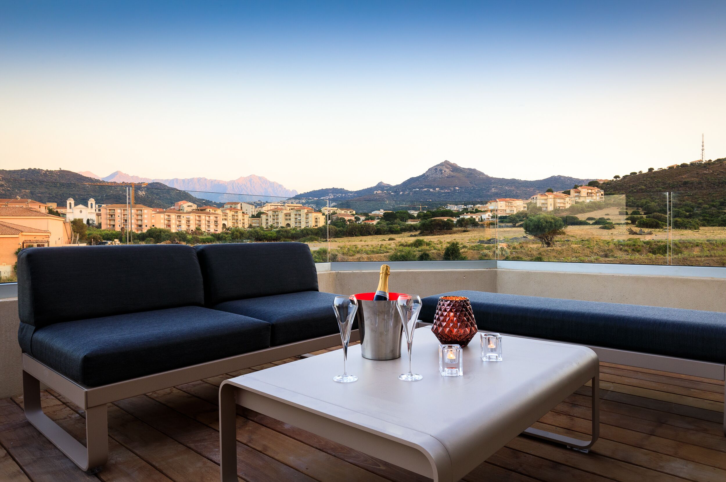 A balcony with a sofa, a table, and a bottle of champagne.