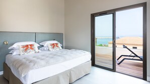 Een slaapkamer met een groot bed, uitzicht op zee door een schuifdeur en een balkon met een stoel.