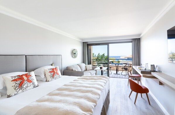 A modern hotel room with a large bed, a sofa, a dining table, and a balcony with a view.