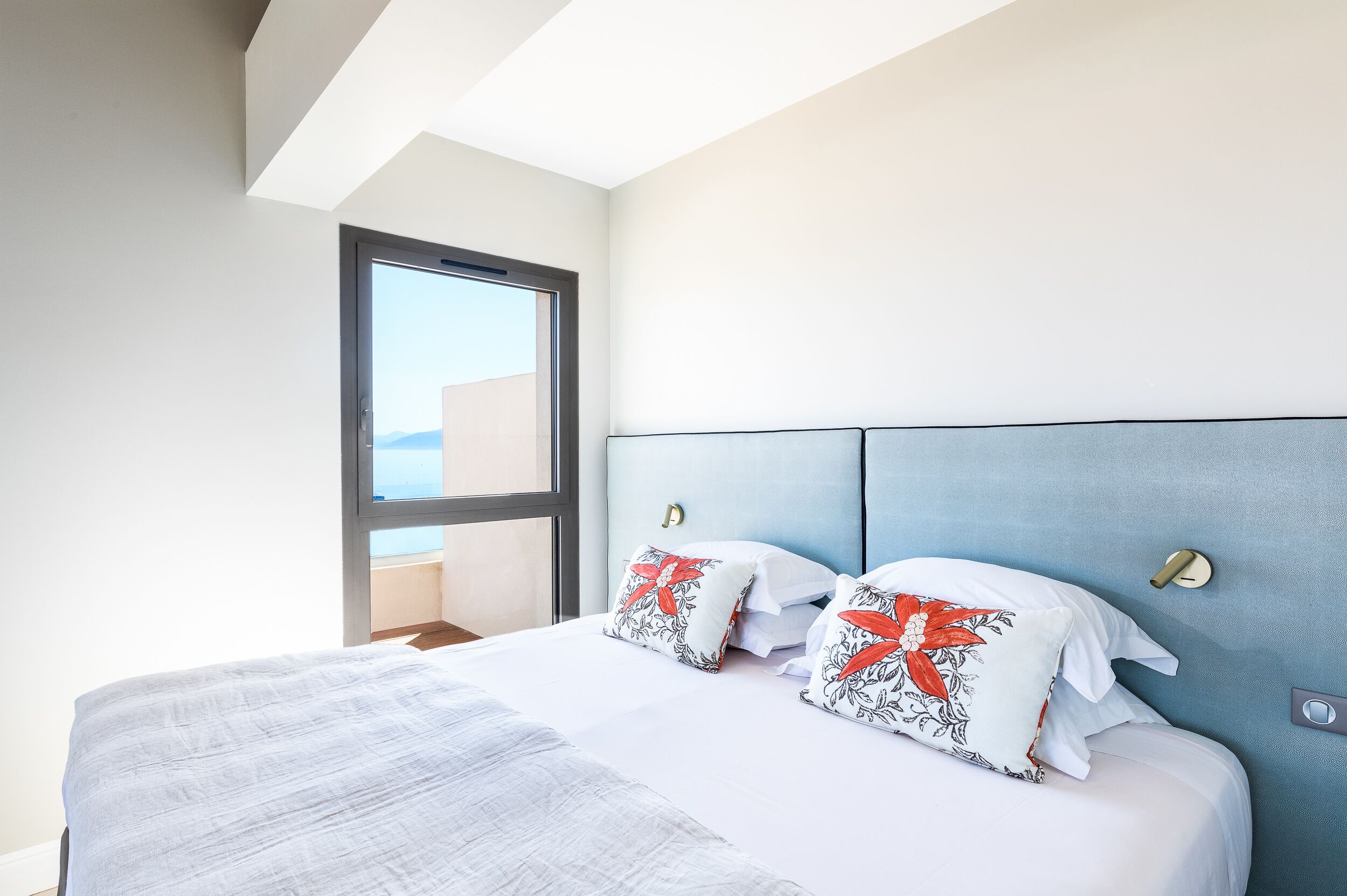 Una habitación de hotel moderna con una cama grande, vistas al mar a través de una ventana y una pared de acento azul.