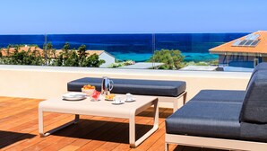 A balcony with a table set for breakfast, a cushioned seating area, and a view of the sea.
