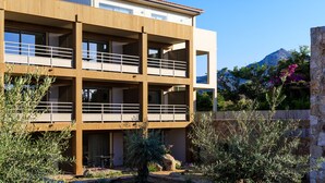 A modern two-story building with balconies, a stone wall, and a mountain in the background.