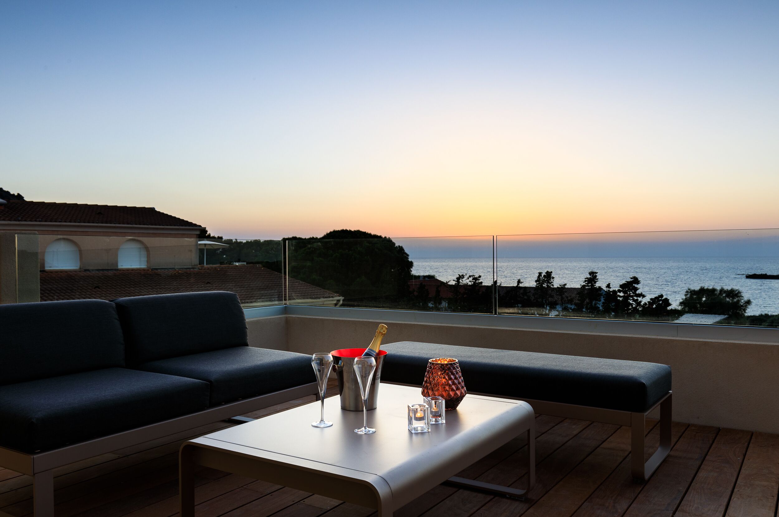 A balcony with a sofa, a table, and a view of the sea at sunset.