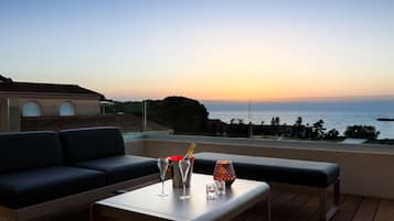 A balcony with a sofa, a table, and a view of the sea at sunset.