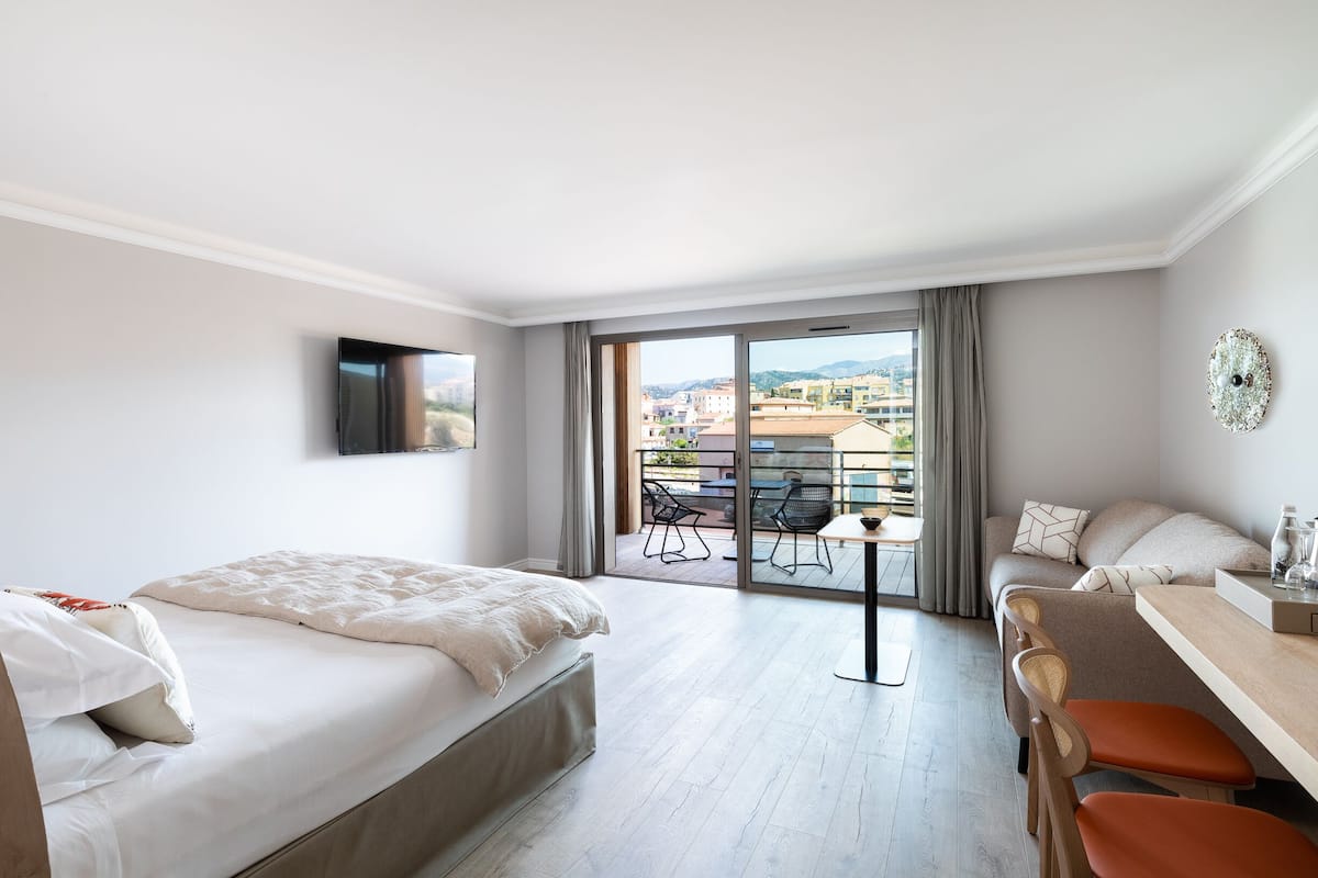 A hotel room with a bed, a desk, and a balcony with a table and chairs.