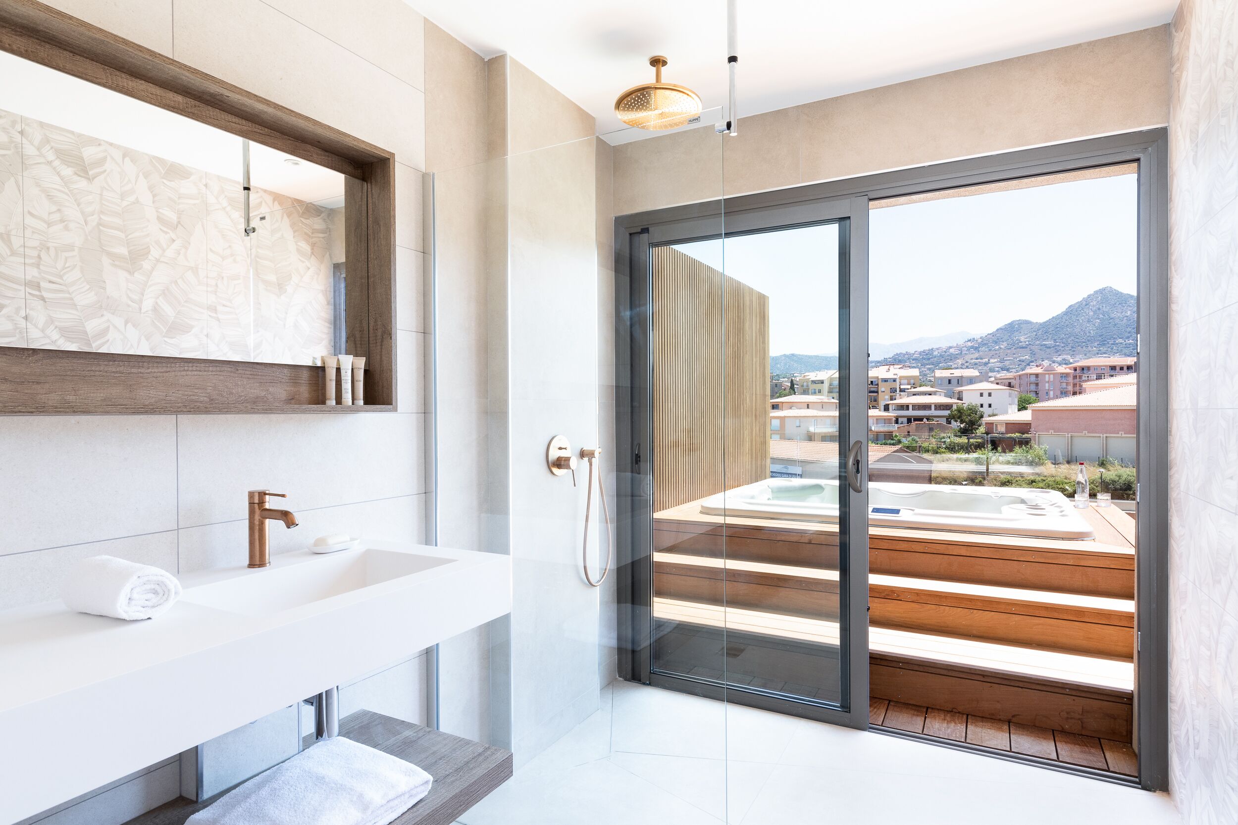 Un bagno moderno con un lavandino ampio, uno specchio e una porta vetrata che dà su un balcone con vasca idromassaggio.