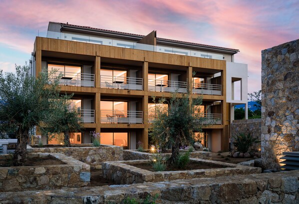 A modern multi-story building with balconies, stone walls, and outdoor lighting.