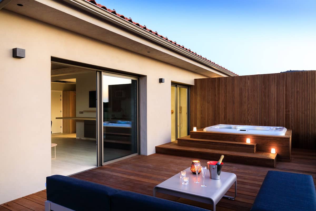 A modern outdoor area with a hot tub, wooden deck, and a glass door leading to a room.