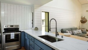 A modern kitchen with white tiled walls, a stainless steel oven, blue cabinets, and a large sink. - Beach & Poolside Bliss - Family-Friendly Maui Stay (Kihei)