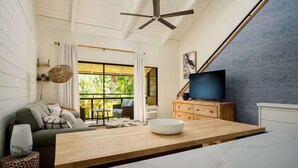 A modern living room with a large wooden table, a sofa, a television, and a ceiling fan. - Beach & Poolside Bliss - Family-Friendly Maui Stay (Kihei)