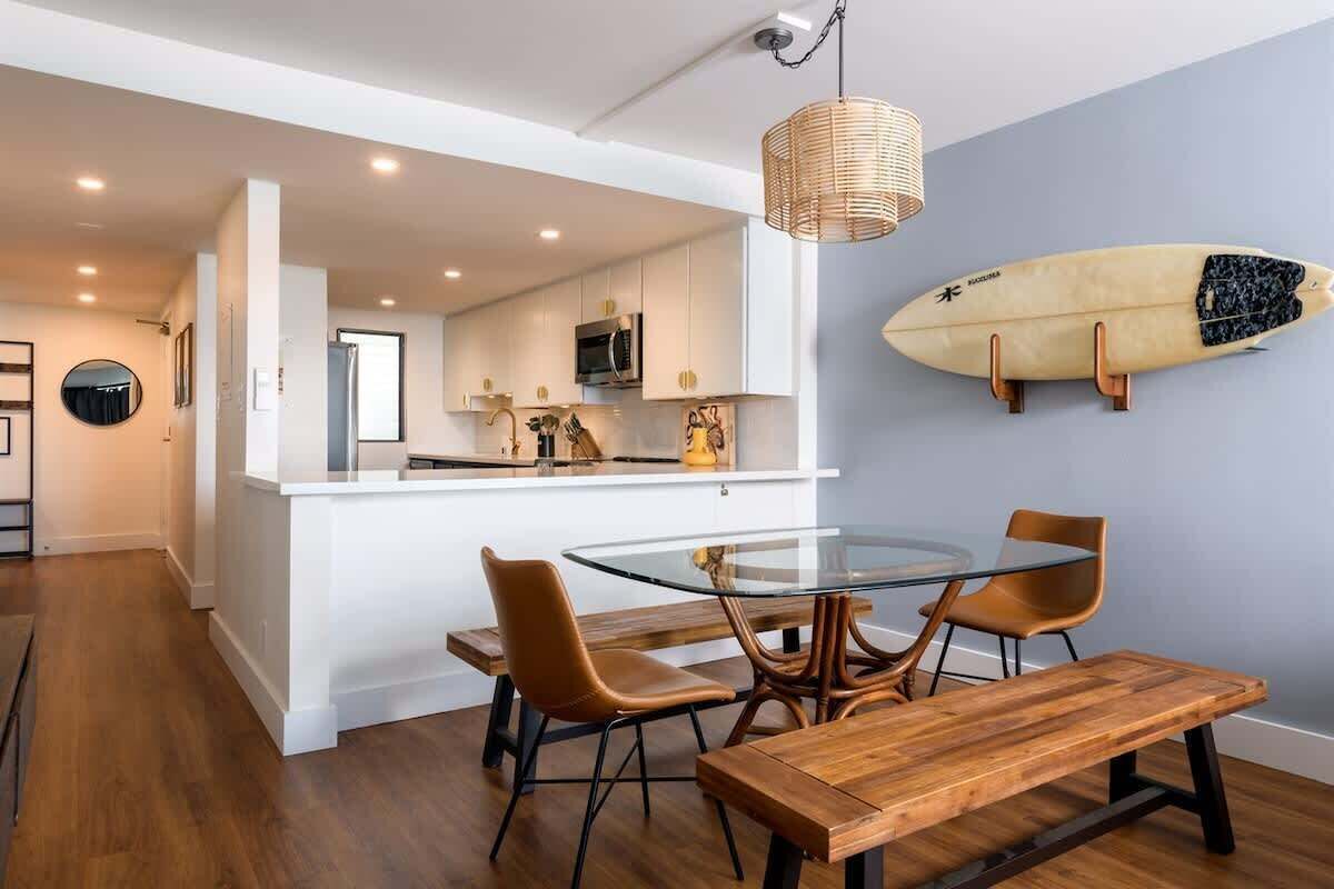 A modern kitchen with white cabinets, a microwave, and a hanging surfboard.