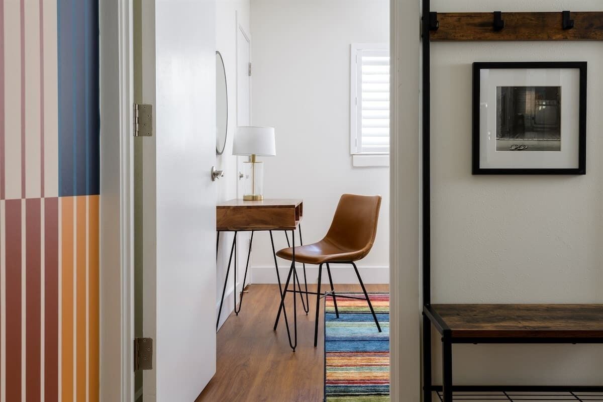 Un couloir avec un plancher en bois, une chaise, une petite table avec une lampe et un tableau encadré au mur.