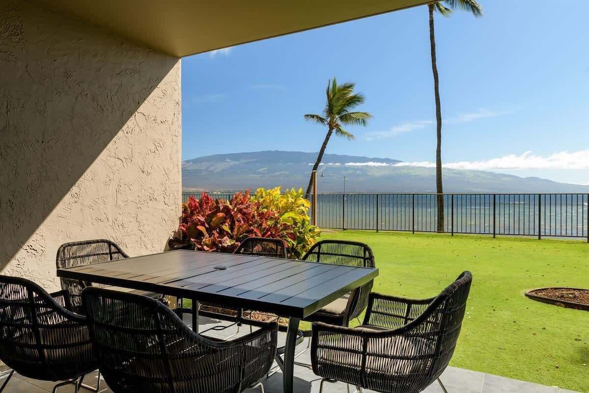 An outdoor patio with a table and chairs, a view of the ocean, and a mountain range in the background.