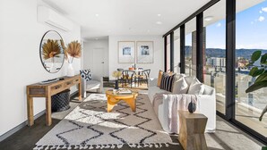 A modern living room with a white sofa, a wooden coffee table, and a large window offering a city view. - Wollongong CBD Ocean View Apartment (Wollongong)