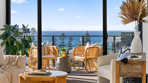 A balcony with wicker furniture, a potted plant, and a view of the sea. - Wollongong CBD Ocean View Apartment (Wollongong)