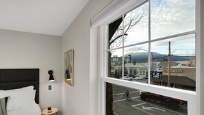 A hotel room with a large window, a bed, a nightstand, and a framed picture on the wall. - Summit Lofts, Mt Shasta, 2 Queen Beds #209 (Mt Shasta)
