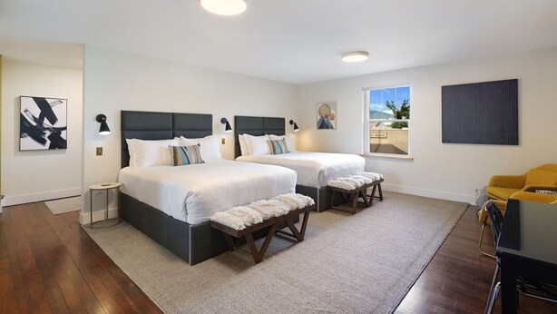 A modern bedroom with two beds, a small side table, a bench, and a view of the outdoors. - Summit Lofts, Mt Shasta, 2 Queen Beds #209 (Mt Shasta)