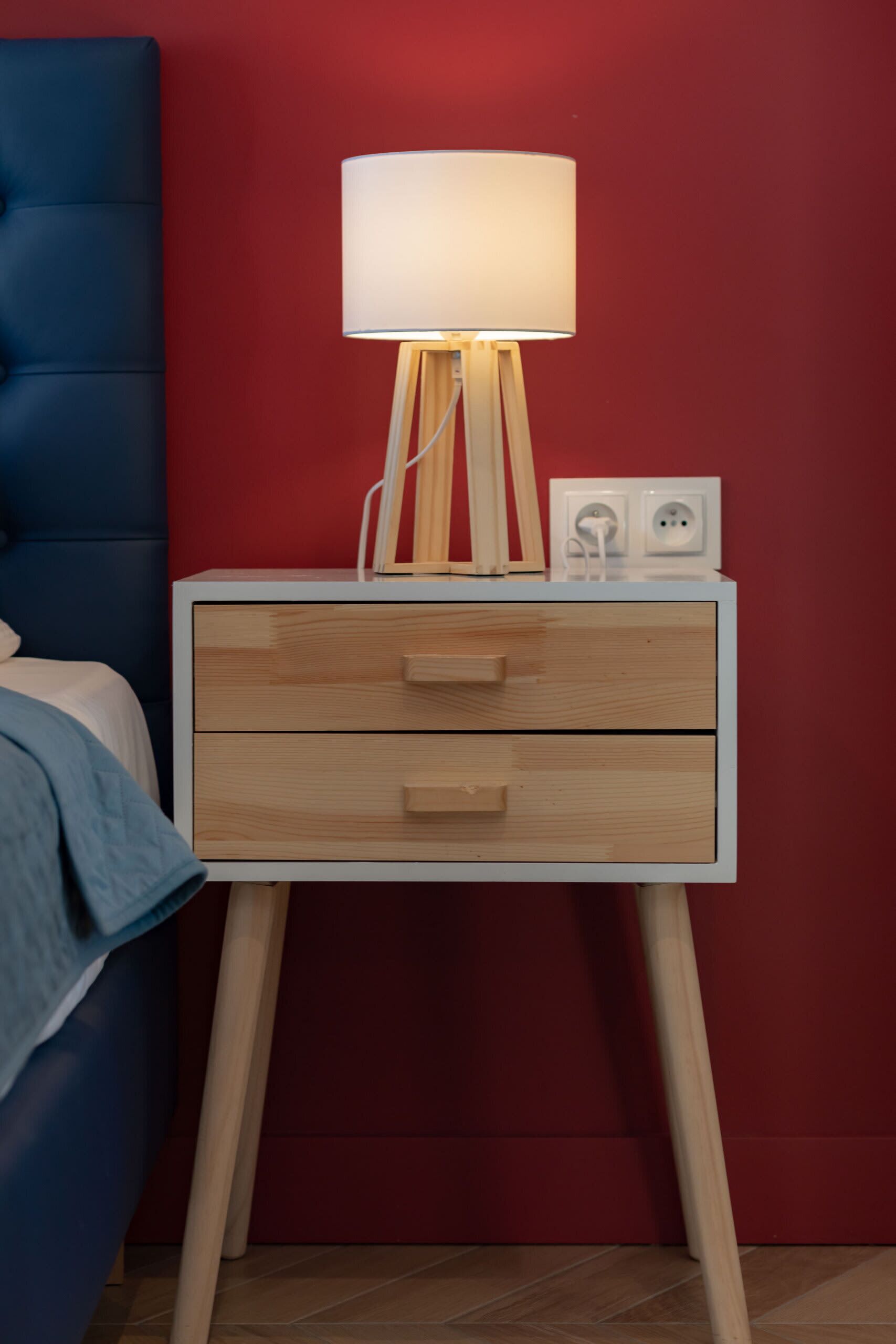 Ein Nachttisch mit Lampe, Steckdose und Schublade.