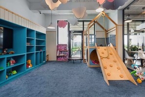 Un espace de jeux pour enfants avec un toboggan, des étagères remplies de jouets et une petite maison.