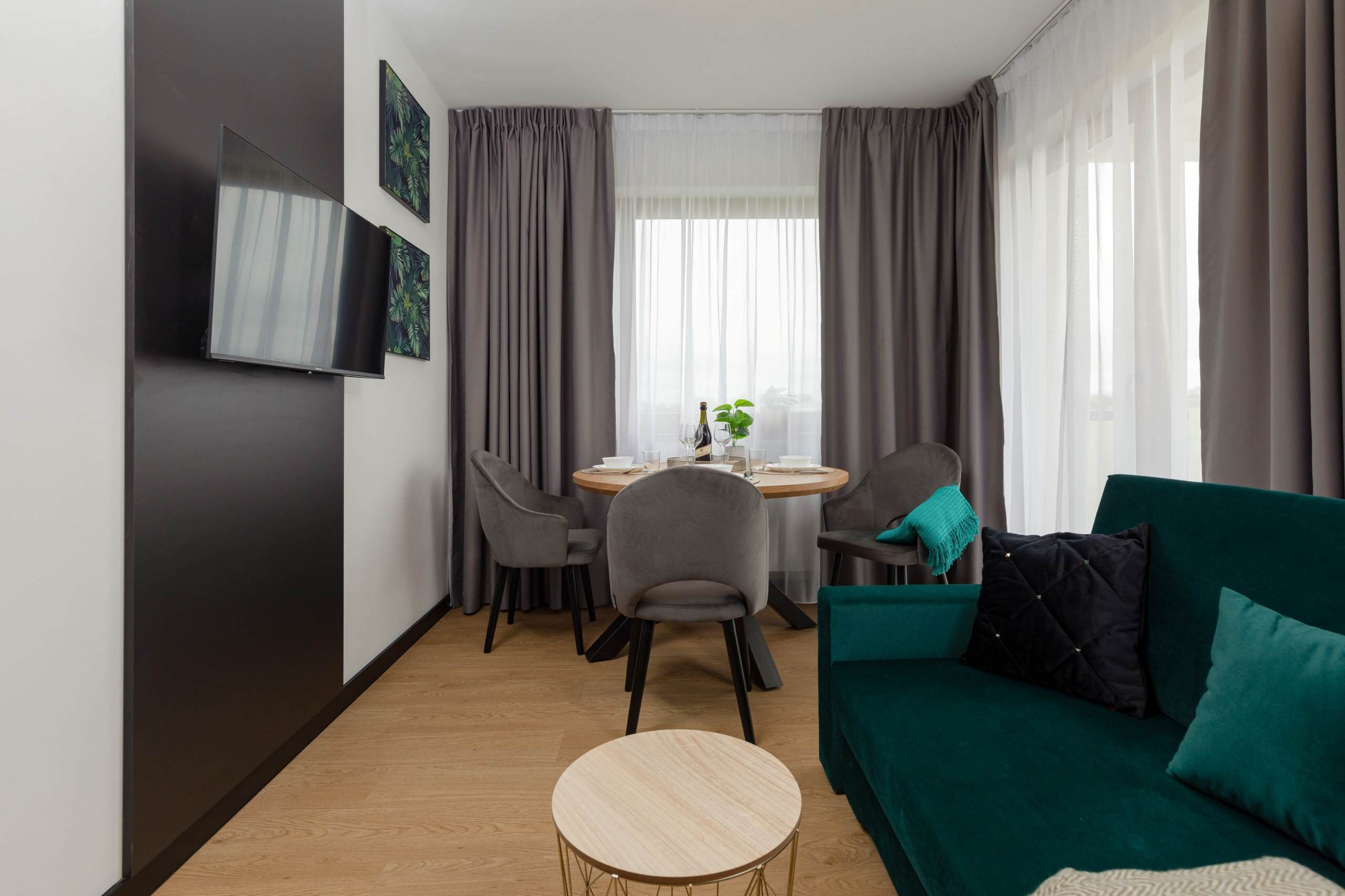 Un salon moderne avec un canapé vert, une table ronde en bois et deux fauteuils gris.
