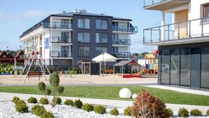 A modern building with multiple balconies, a playground, and a landscaped area with small trees and shrubs. - Air-conditioned Apartment | Swimming Pool in the Property, Close to the Sea (Sarbinowo)