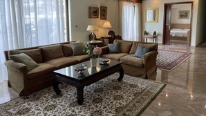 A living room with a sofa, coffee table, and a rug. There is a bed in the background and a door leading to another room. - Athens Neos Kosmos Penthouse, city center & sea view (Athina)