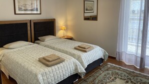 A hotel room with two beds, a wooden headboard, a nightstand with a lamp, and a large window with sheer curtains. - Athens Neos Kosmos Penthouse, city center & sea view (Athina)