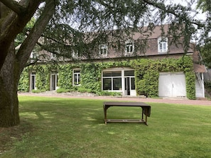 A house with a covered porch, a garage, and a lawn with a bench.
