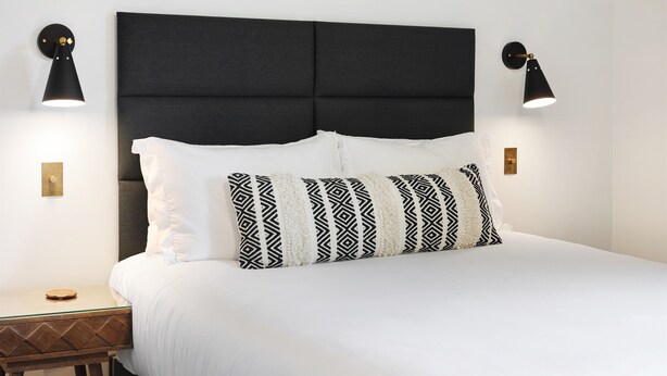 A neatly made bed with a black headboard, two bedside lamps, and a wooden nightstand with a round mirror. - Summit Lofts, Mt Shasta, View of Lava Dome Volcano #208 (Mt Shasta)