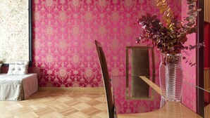 Ein Zimmer mit geprägter rosa Tapete, einer klaren Vase mit Trockenblättern und einem Holzboden.