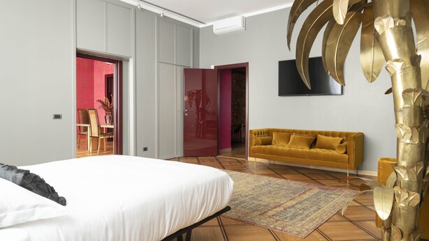 Ein modernes Schlafzimmer mit einem Bett, einer Couch, einem Fernseher und einer großen Pflanze.
