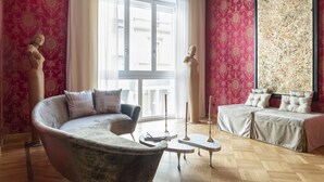 Ein modernes Wohnzimmer mit einer gebogenen Couch, einem Zweisitzer-Sofa und einem Couchtisch. Auf dem Couchtisch stehen zwei hohe Kerzen.