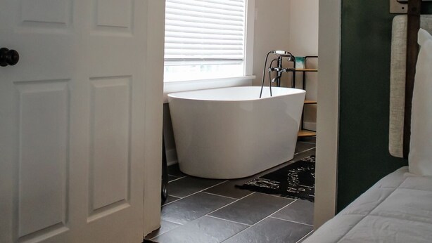 Ein Badezimmer mit freistehender Badewanne, einem Fenster mit Jalousien und einer Tür zu einem anderen Raum.
