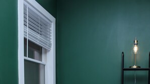 Ein Zimmer mit einem dunkelgrauen Sofa, einem Korbwannen, einem weißen Fenster mit Jalousien und einem schwarzen Metallregal mit Körben.