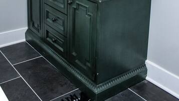 A bathroom with a dark green vanity, a round mirror, and a white sink.