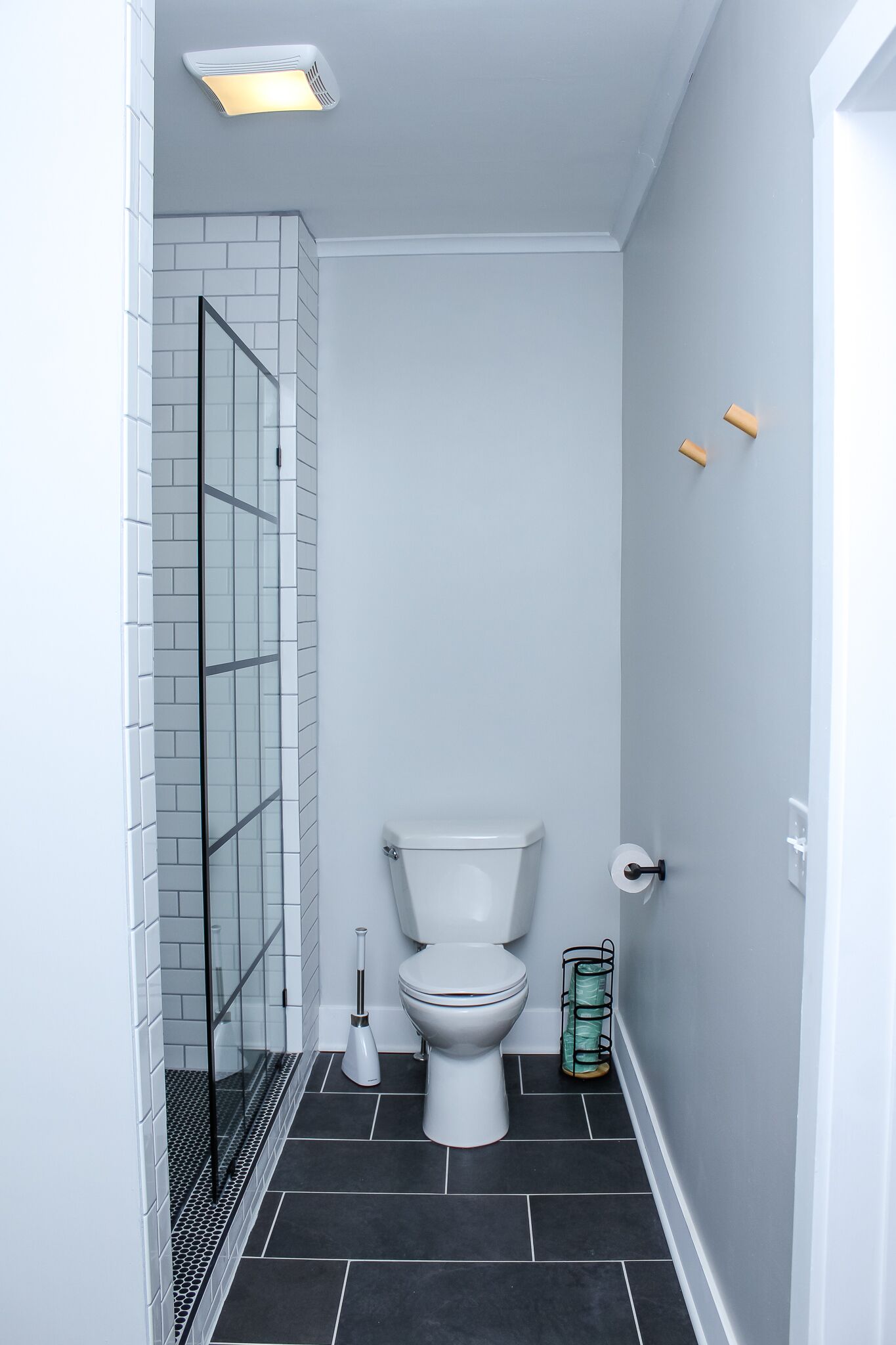 A bathroom with a toilet, a glass shower enclosure, and a toilet brush.