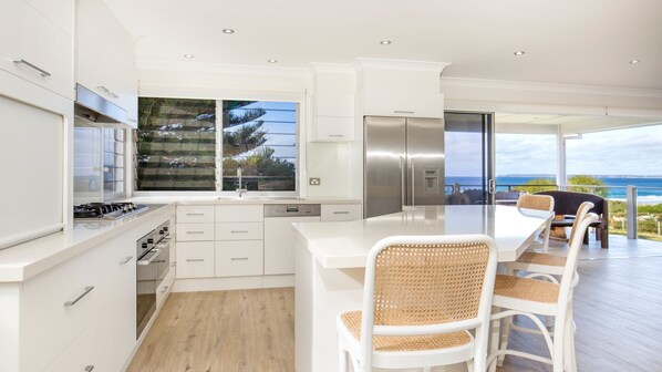 A modern kitchen with white cabinetry, a stainless steel refrigerator, and a large window overlooking a scenic view.