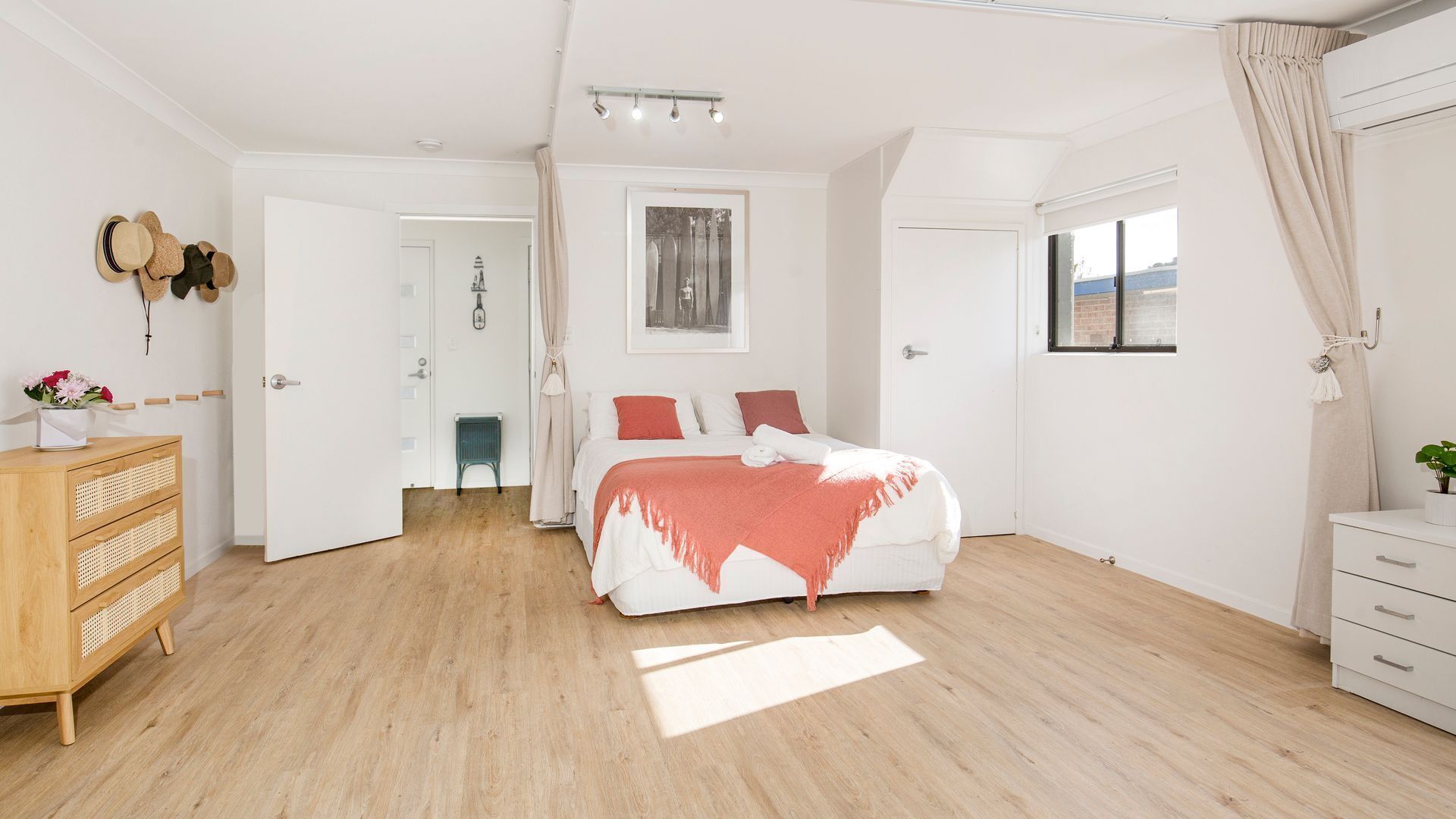 A bedroom with a bed, a wooden dresser, a chair, and a window with curtains.