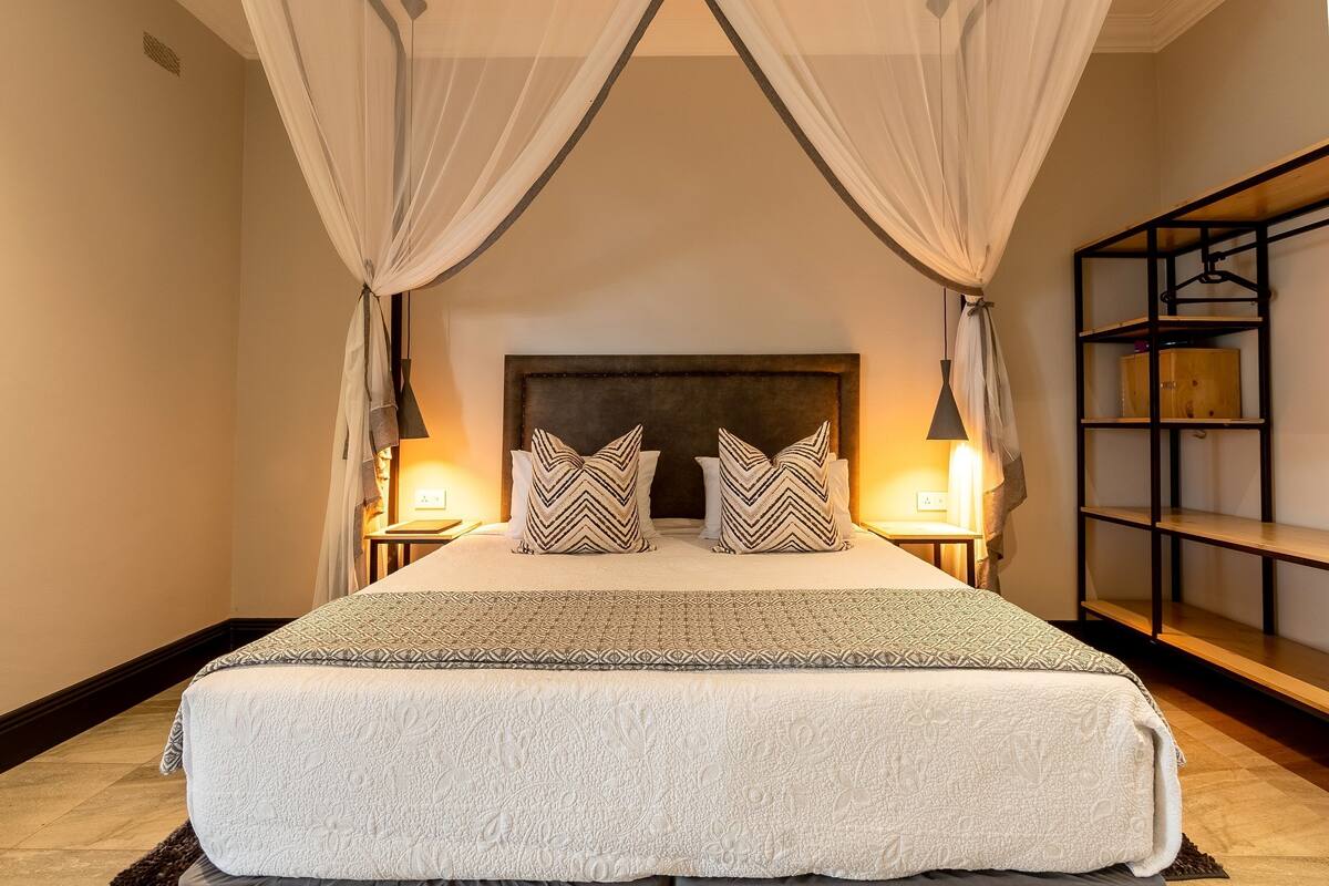 A neatly made bed with a patterned bedspread and pillows, a headboard, bedside lamps, and a bookshelf.